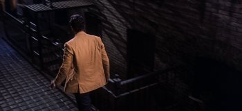 Movie still from “West Side Story” (1961), directed by Jerome Robbins – A man wearing a jacket walking down the side of a building; Wide shot, High angle