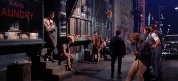 Movie still from “West Side Story” (1961), directed by Jerome Robbins – A group of men sitting on steps in front of a building; Wide shot, High angle