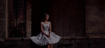 Movie still from “West Side Story” (1961), directed by Jerome Robbins – A young woman in a white dress sitting on a ledge; Wide shot, Low angle