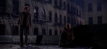 Movie still from “West Side Story” (1961), directed by Jerome Robbins – A woman sitting on the ground in front of a building; Wide shot, High angle