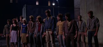 Movie still from “West Side Story” (1961), directed by Jerome Robbins – A group of young men standing next to each other in front of a chain link fence at night; Wide shot, Low angle