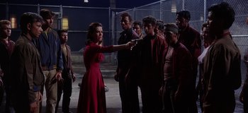 Movie still from “West Side Story” (1961), directed by Jerome Robbins – A group of people standing around a woman holding a knife; Medium shot, Over the shoulder angle