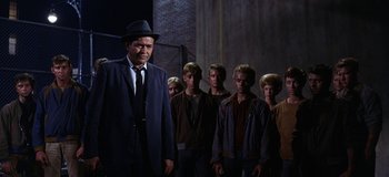 Movie still from “West Side Story” (1961), directed by Jerome Robbins – A man in a suit standing in front of a group of young men; Medium shot, Low angle