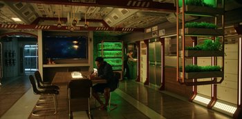 Movie still from “Another Life” (2019), created by Aaron Martin – A man sitting at a table in a room; Wide shot, High angle