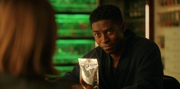 Movie still from “Another Life” (2019), created by Aaron Martin – A man sitting at a table holding a bag of food; Close Up shot, Over the shoulder angle