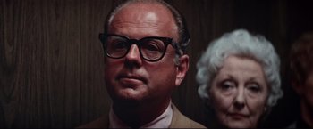 Movie still from “Westworld” (1973), directed by Michael Crichton – An older man wearing glasses and wearing a suit; Close Up shot, Low angle