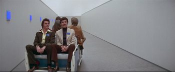 Movie still from “Westworld” (1973), directed by Michael Crichton – A man sitting on a bench in front of a white wall; Wide shot, Low angle