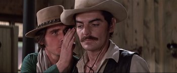 Movie still from “Westworld” (1973), directed by Michael Crichton – A man in a cowboy hat is touching the ear of another man in a cowboy hat; Close Up shot, Over the shoulder angle