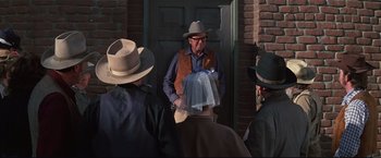 Movie still from “Westworld” (1973), directed by Michael Crichton – A man wearing a hat standing in front of a group of people; Medium shot, Over the shoulder angle