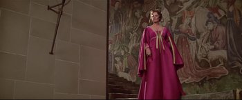 Movie still from “Westworld” (1973), directed by Michael Crichton – A woman in a pink dress standing in front of a mural; Wide shot, Low angle
