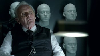 Movie still from “Westworld” (2016), created by Lisa Joy – A man sitting in front of a group of heads in a room; Close Up shot, Over the shoulder angle