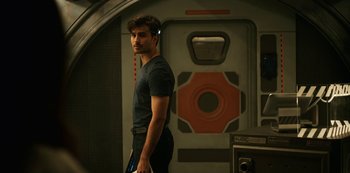 Movie still from “Another Life” (2019), created by Aaron Martin – A man standing next to a door in a room; Medium shot, Over the shoulder angle