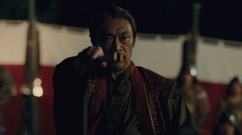 Movie still from “Westworld” (2016), created by Lisa Joy – An older man holding a knife in his mouth; Medium shot, Over the shoulder angle