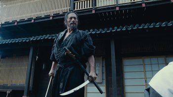 Movie still from “Westworld” (2016), created by Lisa Joy – A man holding two swords in front of a building; Medium shot, Low angle