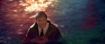 Movie still from “What Dreams May Come” (1998), directed by Vincent Ward – A man wearing a suit and tie sitting in front of a colorful background; Close Up shot, Overhead angle
