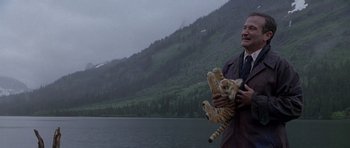 Movie still from “What Dreams May Come” (1998), directed by Vincent Ward – A man holding a baby tiger near a body of water; Medium shot, Low angle