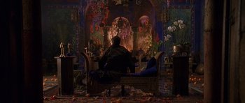 Movie still from “What Dreams May Come” (1998), directed by Vincent Ward – A man sitting on a bench in front of a fire place; Wide shot, Over the shoulder angle