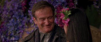 Movie still from “What Dreams May Come” (1998), directed by Vincent Ward – A man smiling while holding a flower in his hand; Close Up shot, Over the shoulder angle