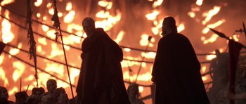 Movie still from “What Dreams May Come” (1998), directed by Vincent Ward – Two men standing next to each other in front of a fire; Medium shot, Low angle