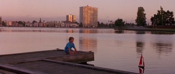 Movie still from “What Dreams May Come” (1998), directed by Vincent Ward – A boy sitting on a dock near a body of water; Wide shot, Low angle