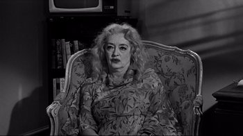 Movie still from “What Ever Happened to Baby Jane?” (1962), directed by Robert Aldrich – An older woman sitting in a chair in front of a television; Medium shot, High angle