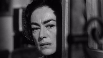 Movie still from “What Ever Happened to Baby Jane?” (1962), directed by Robert Aldrich – An older woman looking sad while standing in front of a window; Close Up shot, Over the shoulder angle