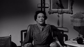 Movie still from “What Ever Happened to Baby Jane?” (1962), directed by Robert Aldrich – An older woman sitting in a chair in front of a painting; Medium shot, Low angle