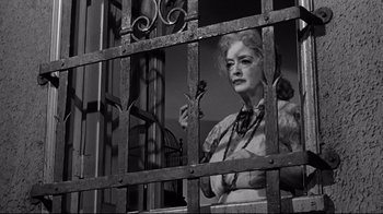 Movie still from “What Ever Happened to Baby Jane?” (1962), directed by Robert Aldrich – An older woman standing behind a metal fence; Medium shot, Low angle