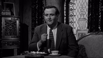 Movie still from “What Ever Happened to Baby Jane?” (1962), directed by Robert Aldrich – A black and white photo of a man sitting at a table; Medium shot, Low angle