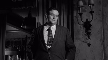 Movie still from “What Ever Happened to Baby Jane?” (1962), directed by Robert Aldrich – Black and white photograph of a man wearing a suit and tie; Medium shot, Low angle