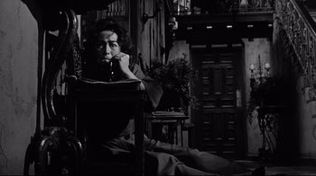 Movie still from “What Ever Happened to Baby Jane?” (1962), directed by Robert Aldrich – An older woman sitting at a table in a room; Medium shot, Low angle
