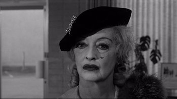 Movie still from “What Ever Happened to Baby Jane?” (1962), directed by Robert Aldrich – An older woman wearing a black hat with a flower on it; Close Up shot, Over the shoulder angle