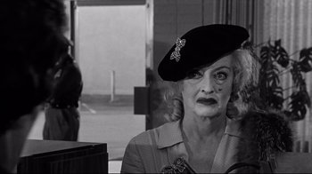 Movie still from “What Ever Happened to Baby Jane?” (1962), directed by Robert Aldrich – An older woman wearing a black hat with a cross on it's brim; Close Up shot, Over the shoulder angle