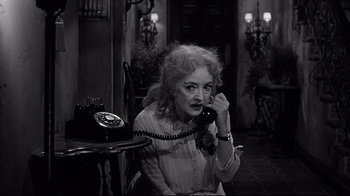 Movie still from “What Ever Happened to Baby Jane?” (1962), directed by Robert Aldrich – An older woman sitting at a table talking on a phone; Medium shot, High angle