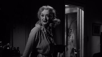 Movie still from “What Ever Happened to Baby Jane?” (1962), directed by Robert Aldrich – An older woman is walking through a doorway; Medium shot, Low angle