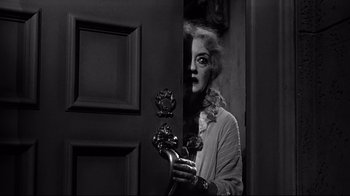 Movie still from “What Ever Happened to Baby Jane?” (1962), directed by Robert Aldrich – A black and white photo of a woman holding a door knob; Medium shot, Over the shoulder angle