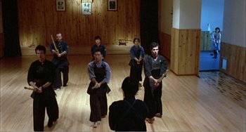 Movie still from “What Have I Done to Deserve This?” (1984), directed by Pedro Almodóvar – A group of people practicing martial arts in a room; Wide shot, High angle