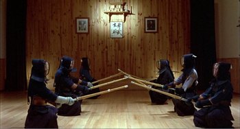 Movie still from “What Have I Done to Deserve This?” (1984), directed by Pedro Almodóvar – A group of people in a room holding wooden sticks; Wide shot, High angle