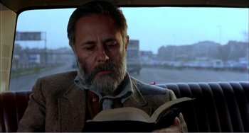 Movie still from “What Have I Done to Deserve This?” (1984), directed by Pedro Almodóvar – An older man reading a book while sitting in a car; Close Up shot, Low angle