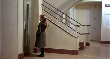Movie still from “What Have I Done to Deserve This?” (1984), directed by Pedro Almodóvar – A woman standing in front of a stair case talking on a cell phone; Wide shot, Over the shoulder angle