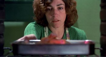 Movie still from “What Have I Done to Deserve This?” (1984), directed by Pedro Almodóvar – A woman sitting in front of a pan of food; Close Up shot, High angle
