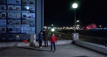 Movie still from “What Have I Done to Deserve This?” (1984), directed by Pedro Almodóvar – A group of people standing on the side of a building at night; Wide shot, Low angle