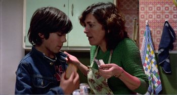 Movie still from “What Have I Done to Deserve This?” (1984), directed by Pedro Almodóvar – A woman and a boy eating a piece of food; Medium shot, Over the shoulder angle