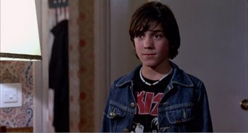 Movie still from “What Have I Done to Deserve This?” (1984), directed by Pedro Almodóvar – A young boy wearing a jean jacket and a kiss shirt; Medium shot, Over the shoulder angle