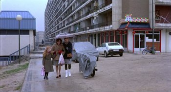 Movie still from “What Have I Done to Deserve This?” (1984), directed by Pedro Almodóvar – Two women and a child are walking in the rain; Wide shot, High angle