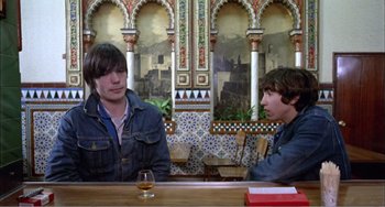 Movie still from “What Have I Done to Deserve This?” (1984), directed by Pedro Almodóvar – Two men sitting at a table with a glass of whiskey; Medium shot, High angle