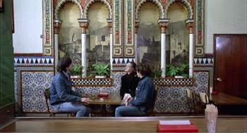 Movie still from “What Have I Done to Deserve This?” (1984), directed by Pedro Almodóvar – A group of people sitting at a table in front of a mural; Wide shot, High angle