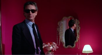 Movie still from “What Have I Done to Deserve This?” (1984), directed by Pedro Almodóvar – A man standing in front of a mirror wearing a suit and tie; Medium shot, Over the shoulder angle