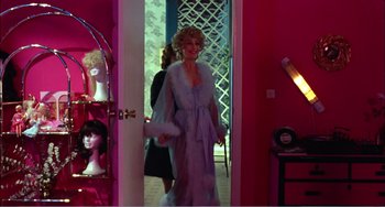 Movie still from “What Have I Done to Deserve This?” (1984), directed by Pedro Almodóvar – A woman in a purple dress standing in front of a mirror; Medium shot, Over the shoulder angle