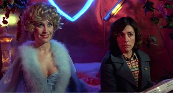 Movie still from “What Have I Done to Deserve This?” (1984), directed by Pedro Almodóvar – Two women are sitting next to each other in front of neon lights; Medium shot, Over the shoulder angle